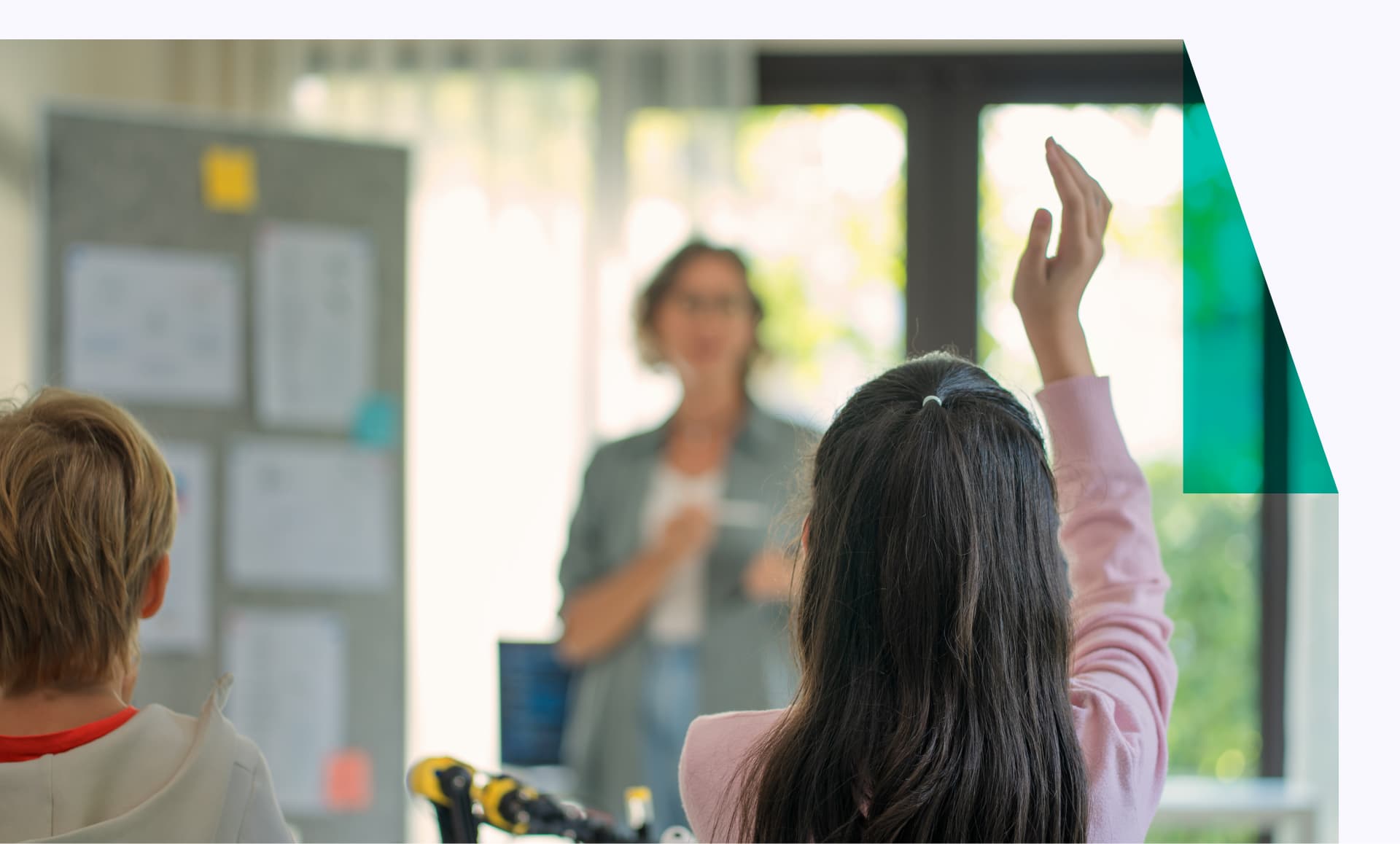 Rear viewpoint of elementary students raising their hands to answer the teacher's question in a class in the STEM classroom.