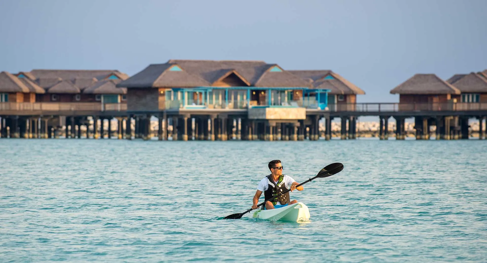 A man kayaking in front of overwater bungalows