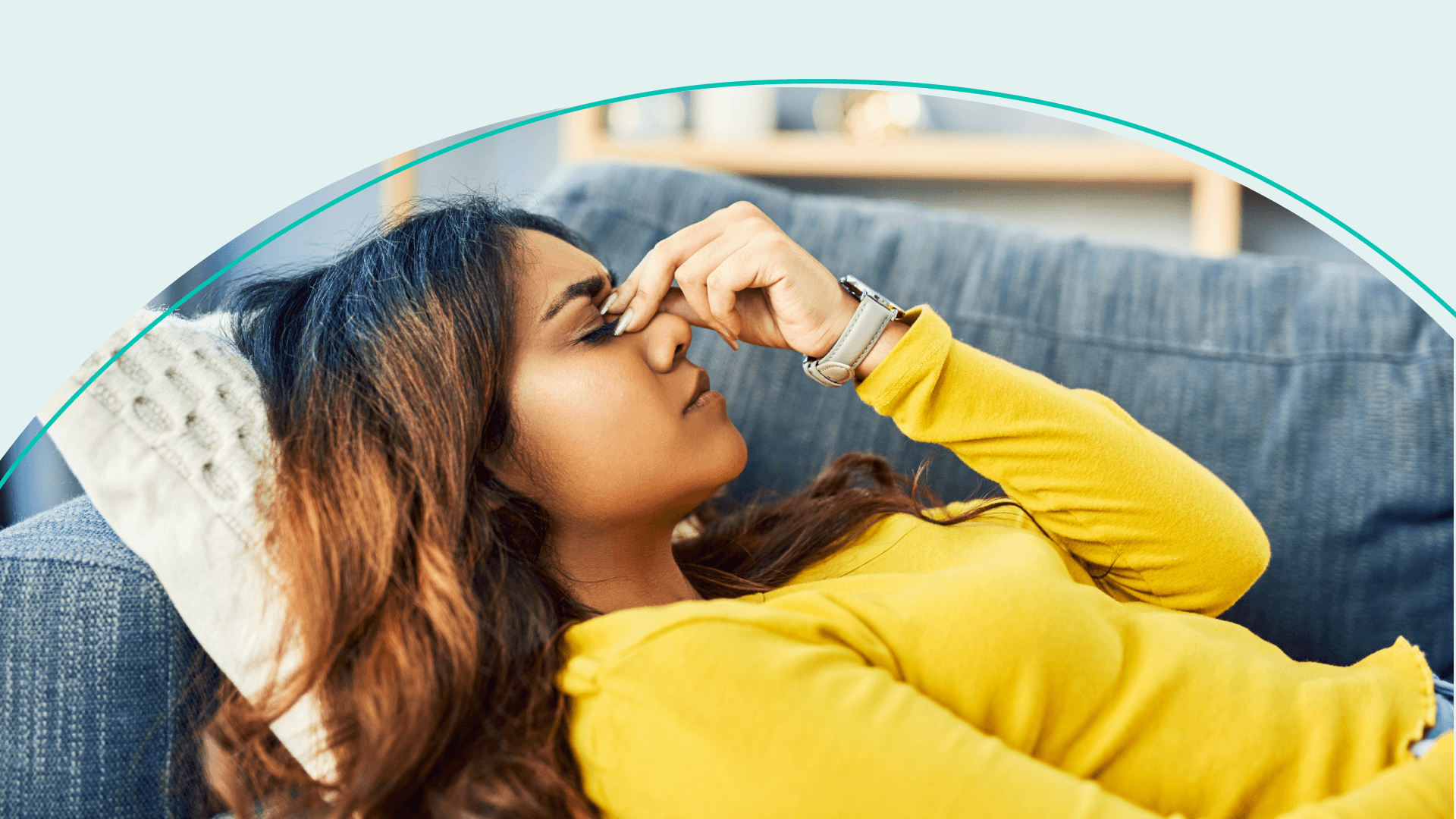 A woman lying on a couch pinching the bridge of her nose