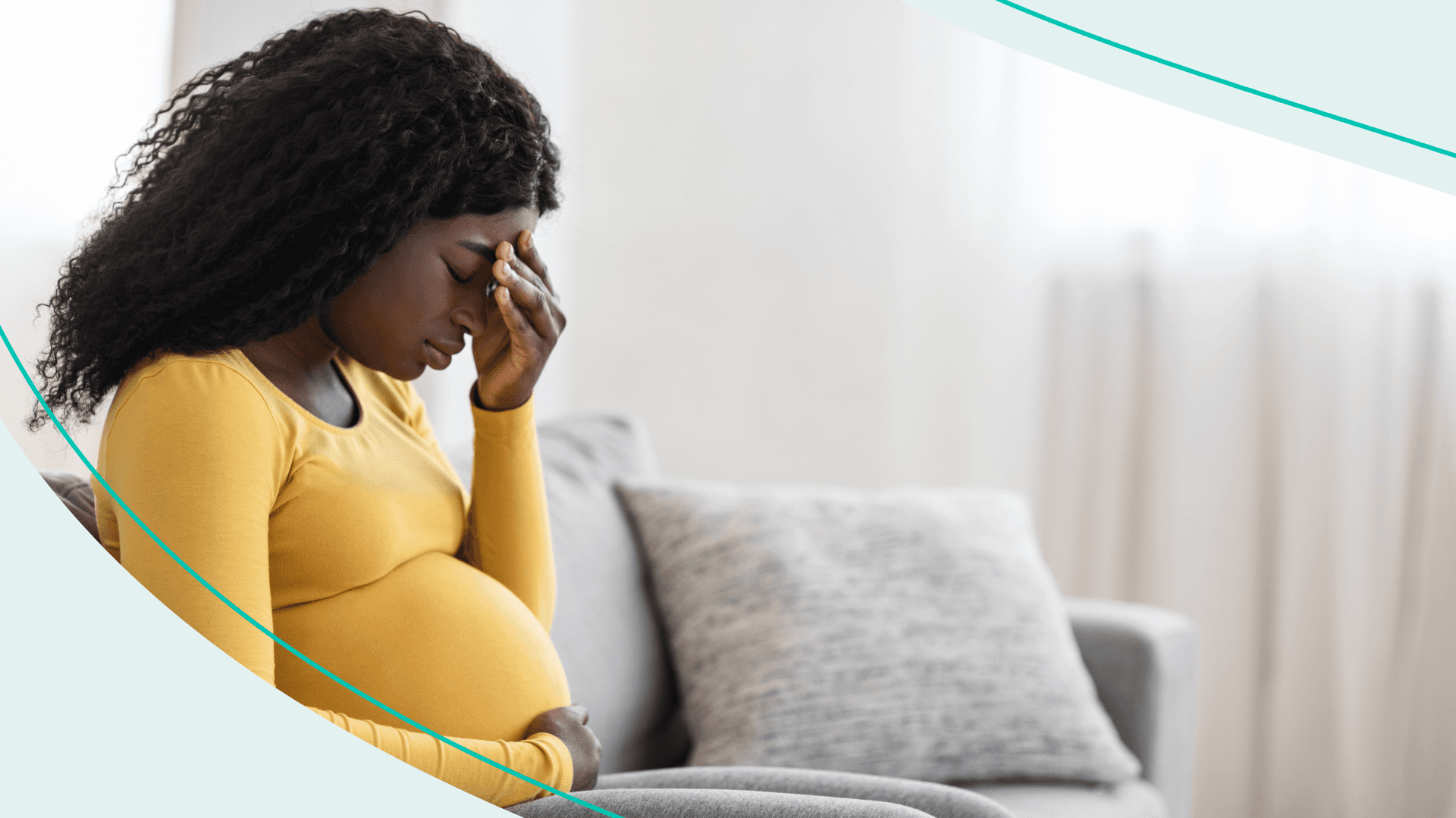 A woman sitting on the couch holding her pregnant belly with her forehead resting on her other hand