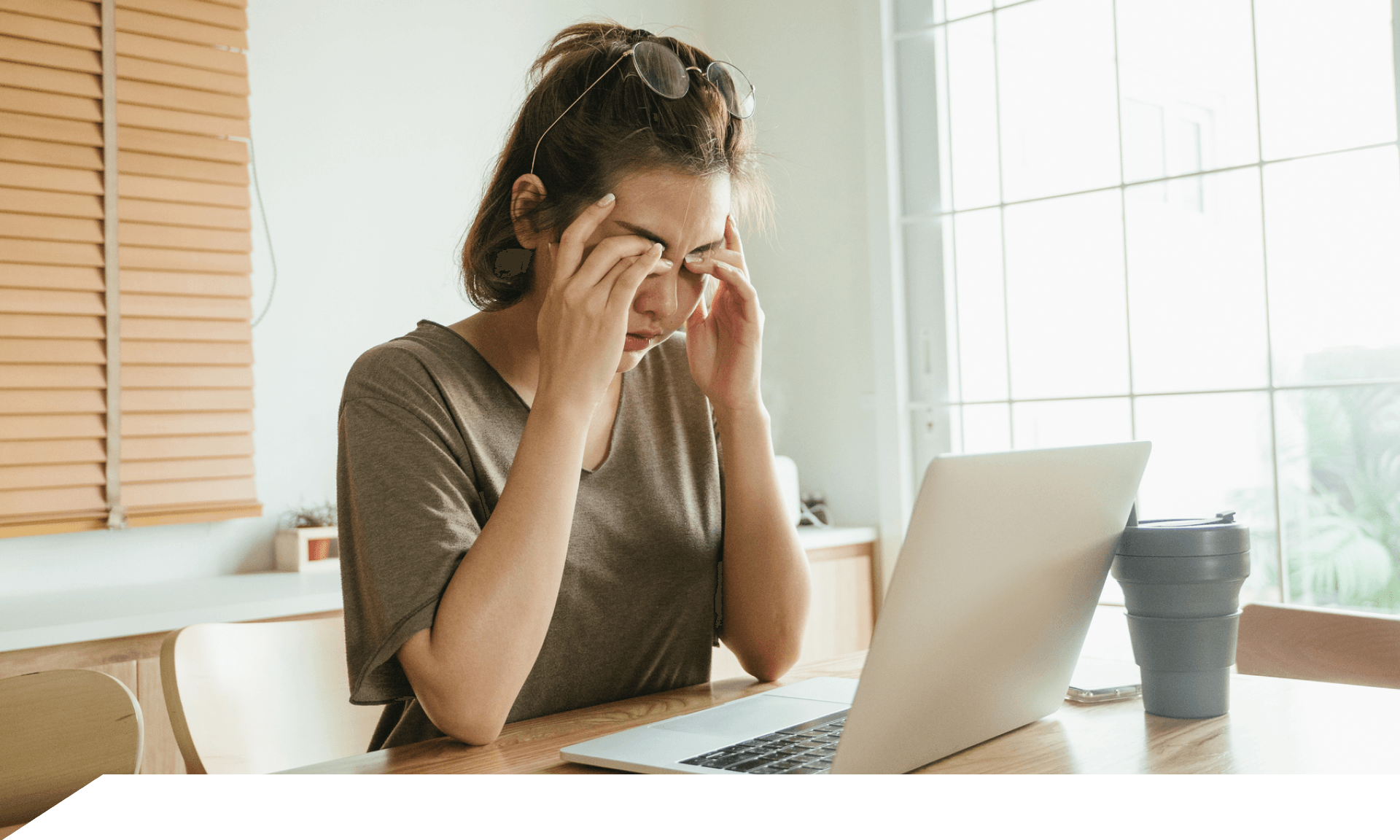 A woman sitting in front of her laptop with her hands covering her eyes
