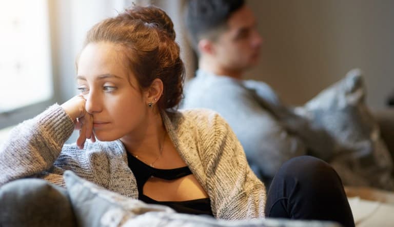 A close-up shot of a young woman looking despondent after a fight with her boyfriend. They are sitting on the couch together but ignoring each other. This photo is being used in an article about relationships fizzling out.