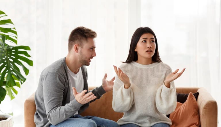 A man and a woman sit on a couch with their hands up as if they