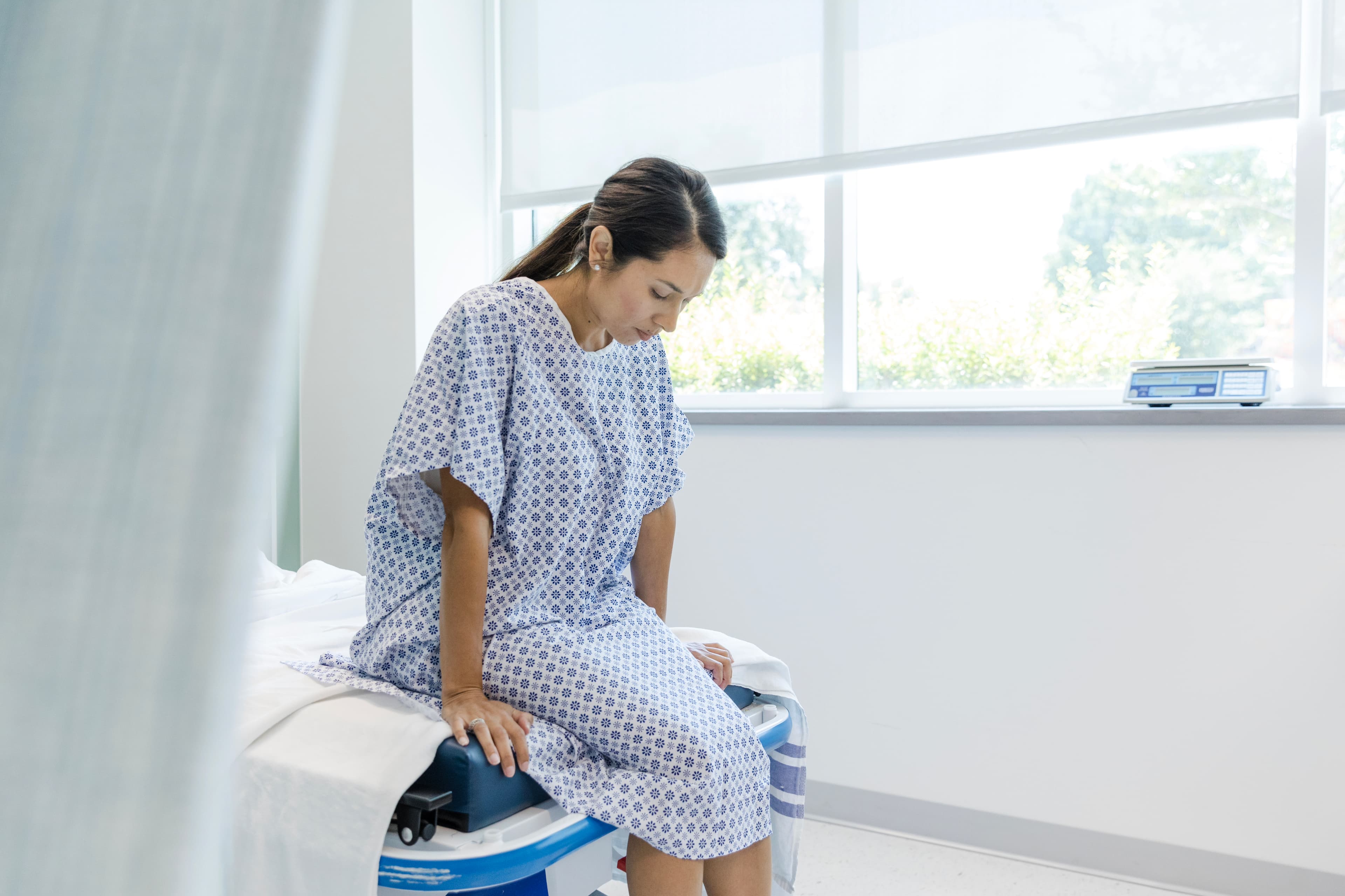 Looking down, woman in hospital gown waits for test results