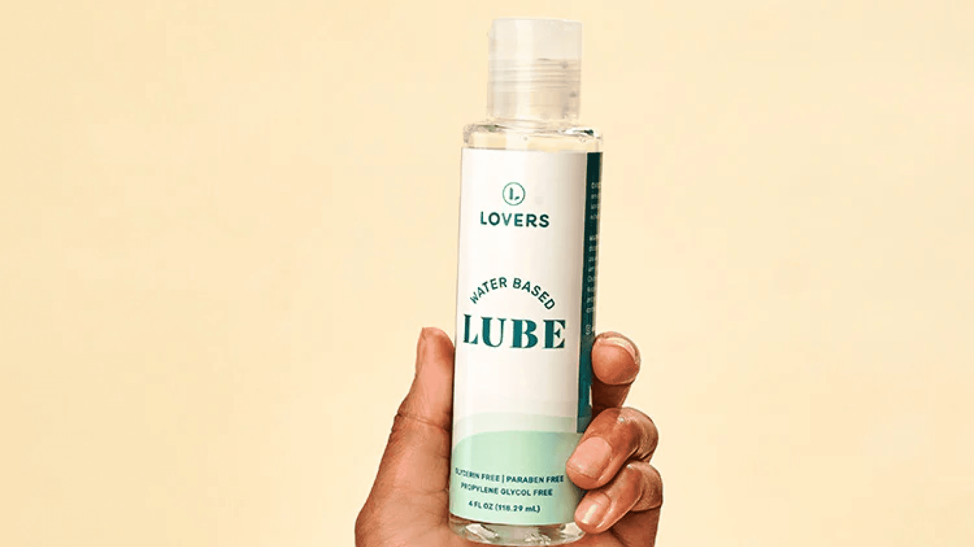 Hand holding bottle of lube with white and green label on pale orange background