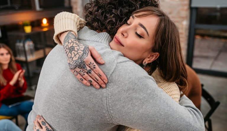 Two people are embracing each other and other members are of a support group are supporting them. The photo is being used to promote an article about the topic