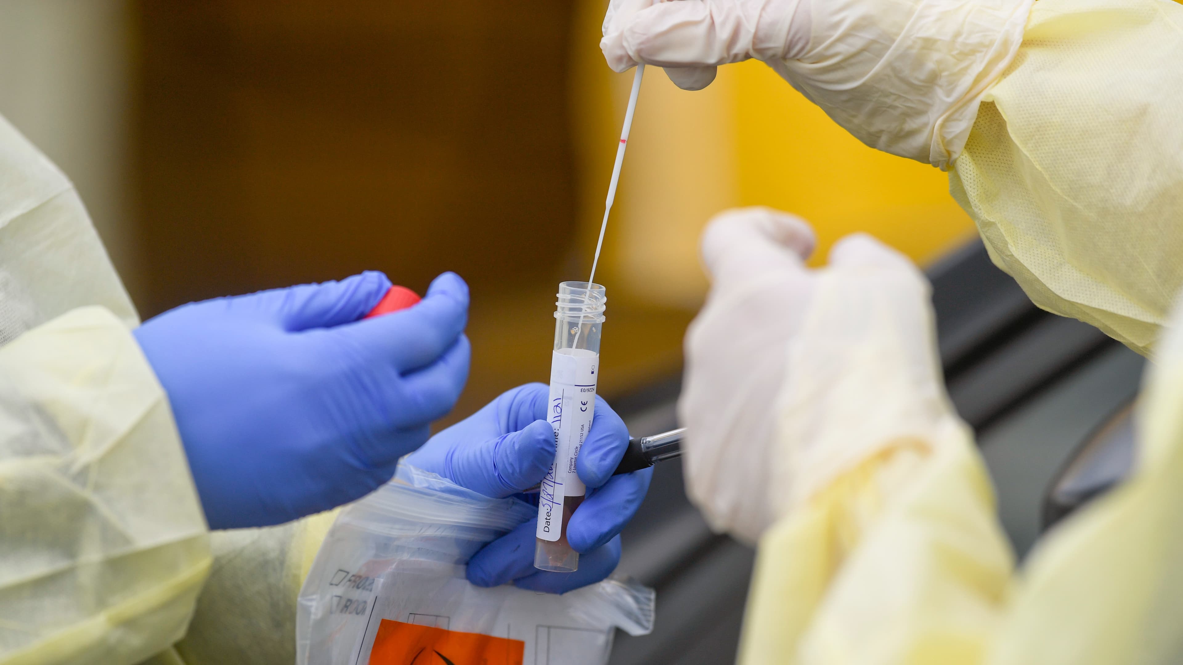 A registered nurse puts a nasal swab into a tube held by another nurse, both wearing gloves and protective gowns, after doing a nasal swab on a patient in their car where they are conducting drive through coronavirus / COVID-19 testing.