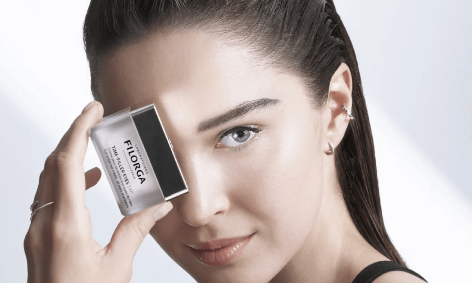 Woman holding opaque eye cream jar in front of her face
